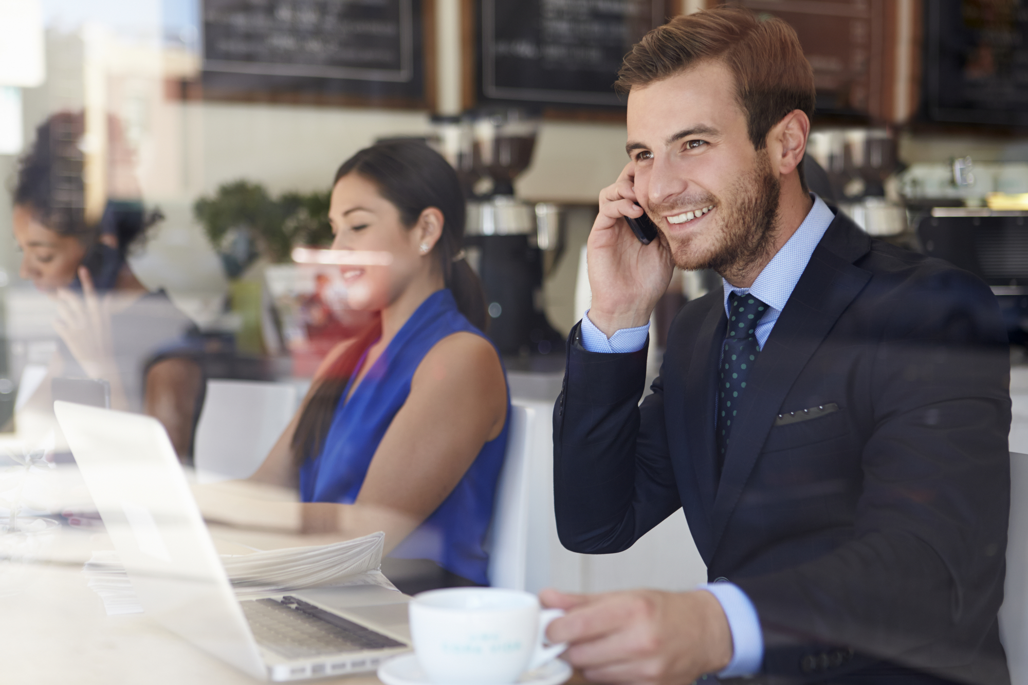 Businessman Using Mobile Phone And Laptop In Coffee Shop