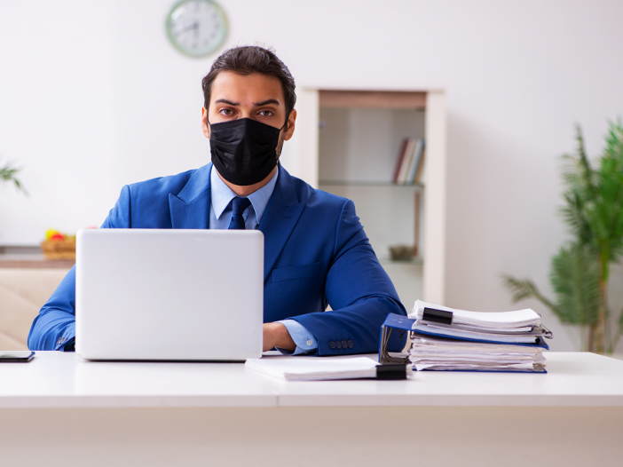 Man working on a laptop with a face mask on IT support 2020 concept.